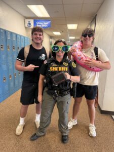 Photo of Deputy Taylor Sullivan with oversized glasses, standing with two high school students