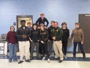 Nick Dean is with surrounded by high school students in a hallway, smiling and posing for the picture